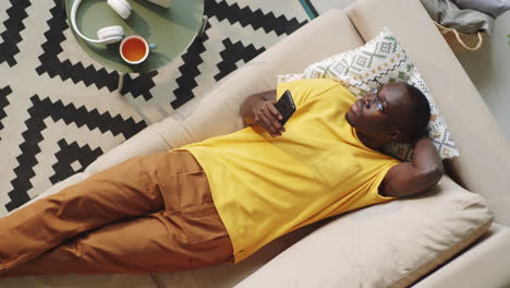Hombre-Negro-Descansando-En-El-Sofá-Con-Teléfono-Inteligente